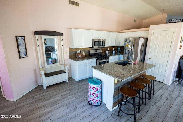 kitchen with appliances with stainless steel finishes, a sink, white cabinets, wood finish floors, and high vaulted ceiling
