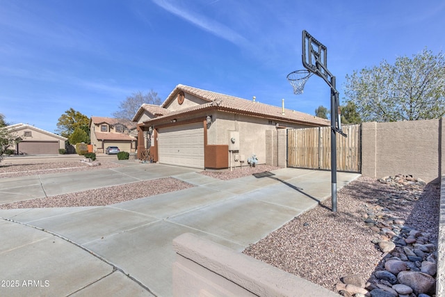 view of side of home with a gate, stucco siding, a tile roof, driveway, and fence