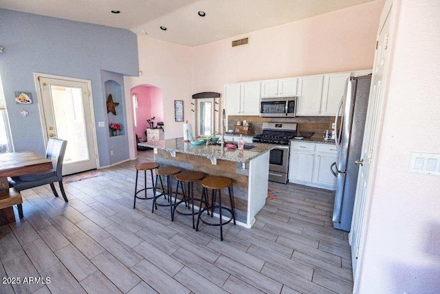 kitchen with appliances with stainless steel finishes, arched walkways, white cabinetry, a kitchen bar, and high vaulted ceiling