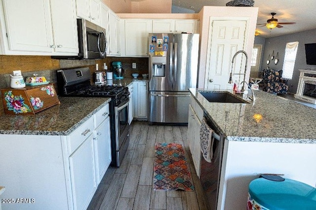 kitchen with appliances with stainless steel finishes, a sink, light wood-type flooring, white cabinets, and stone countertops