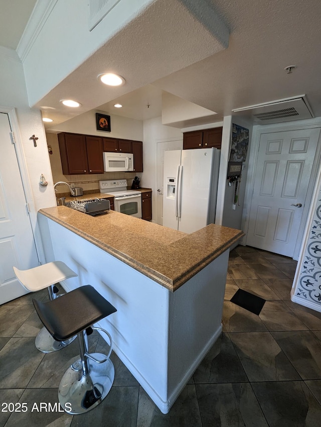 kitchen featuring white appliances, dark brown cabinetry, kitchen peninsula, and a breakfast bar area