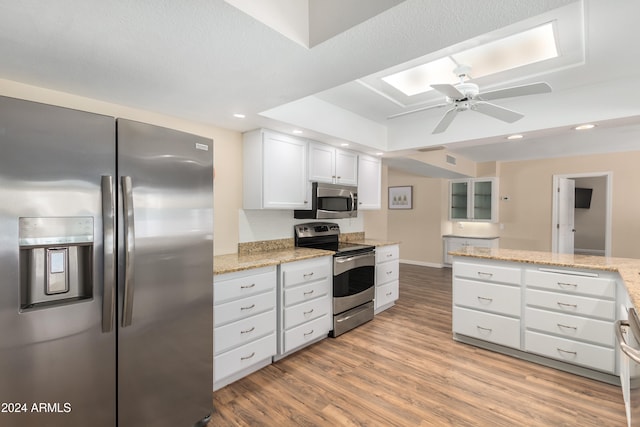 kitchen featuring stainless steel appliances, light hardwood / wood-style floors, white cabinetry, light stone counters, and ceiling fan