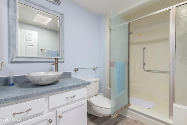 bathroom with wood-type flooring, toilet, vanity, and a shower with shower door