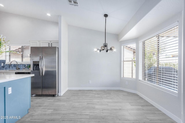 kitchen with pendant lighting, lofted ceiling, light countertops, visible vents, and stainless steel fridge