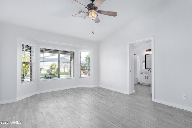 empty room featuring ceiling fan, baseboards, vaulted ceiling, and light wood-style flooring