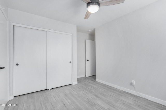 unfurnished bedroom featuring a ceiling fan, a closet, light wood-style flooring, and baseboards