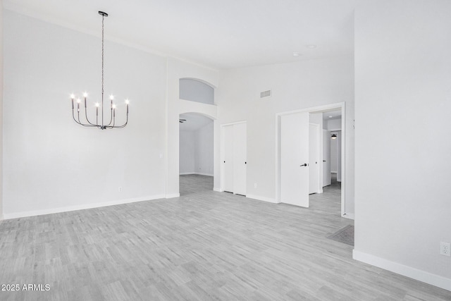 unfurnished room with arched walkways, visible vents, high vaulted ceiling, light wood-type flooring, and baseboards