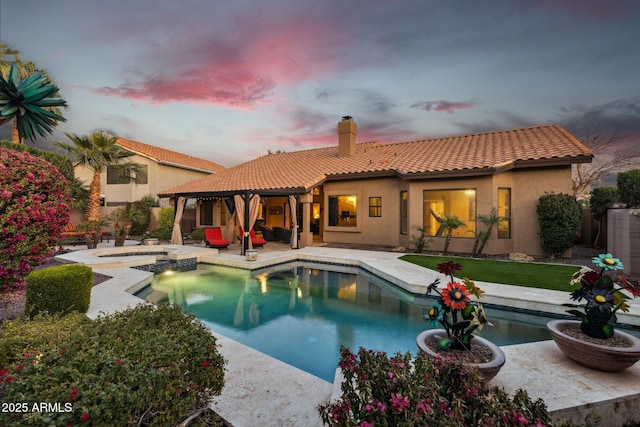 back house at dusk featuring a pool with hot tub and a patio