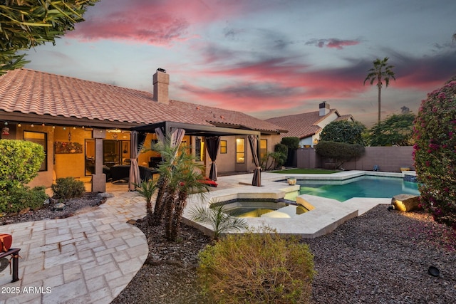 pool at dusk with an in ground hot tub and a patio