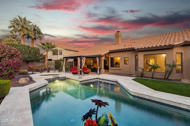 pool at dusk featuring an in ground hot tub and a patio