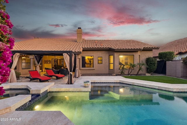 pool at dusk featuring a patio area and an in ground hot tub