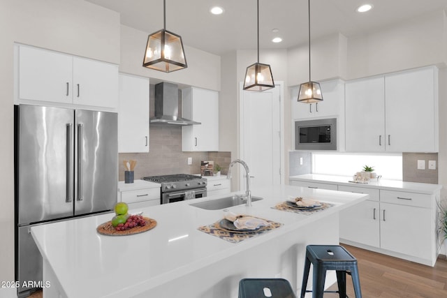 kitchen with a kitchen breakfast bar, stainless steel appliances, wall chimney range hood, sink, and white cabinetry