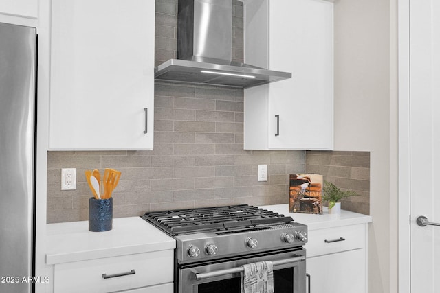 kitchen featuring wall chimney range hood, white cabinetry, stainless steel gas stove, and tasteful backsplash