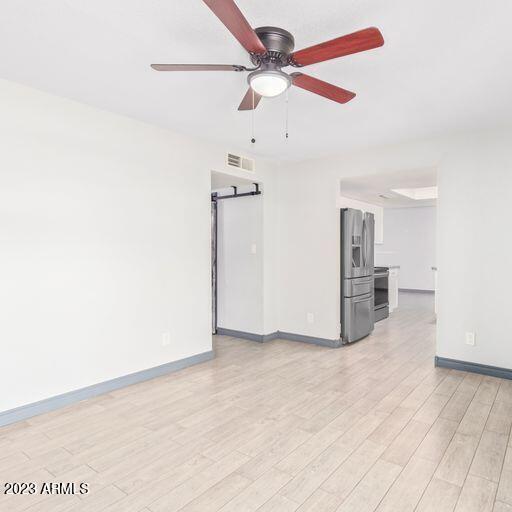 empty room with baseboards, visible vents, light wood finished floors, and a barn door