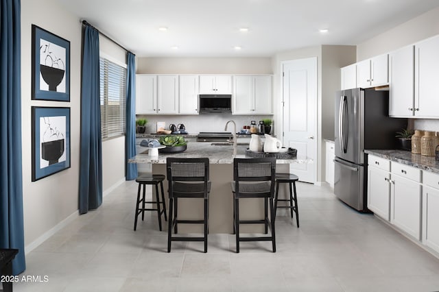 kitchen with appliances with stainless steel finishes, dark stone counters, white cabinets, and a kitchen island with sink