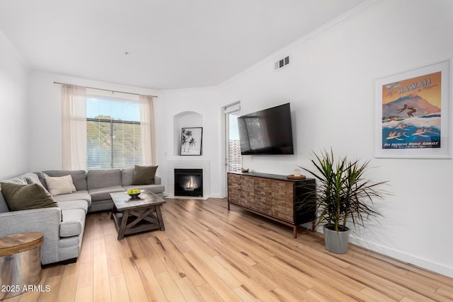 living room with crown molding, a brick fireplace, and light hardwood / wood-style flooring