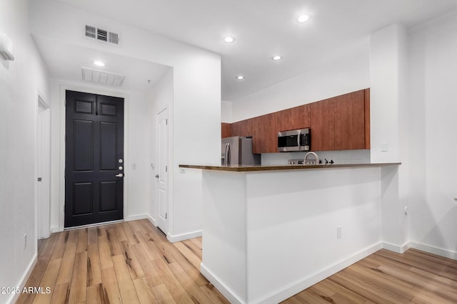 kitchen with light hardwood / wood-style floors, kitchen peninsula, and appliances with stainless steel finishes