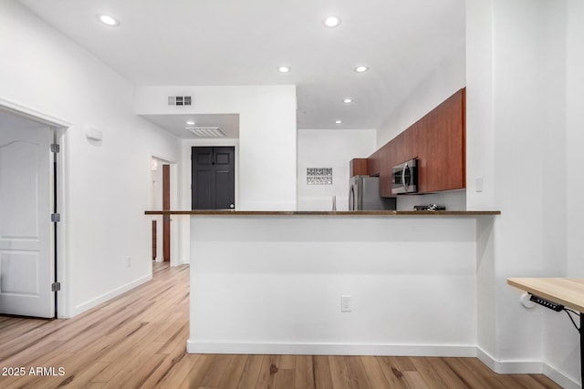 kitchen with stainless steel appliances, kitchen peninsula, and light hardwood / wood-style flooring