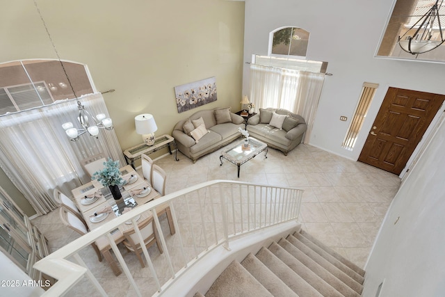 tiled living area with a towering ceiling, a chandelier, stairs, and baseboards