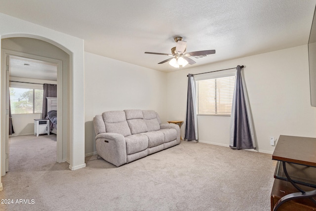 living room with a textured ceiling, ceiling fan, and light carpet