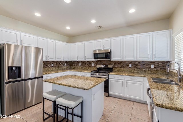 kitchen featuring white cabinets, appliances with stainless steel finishes, stone countertops, sink, and a kitchen island