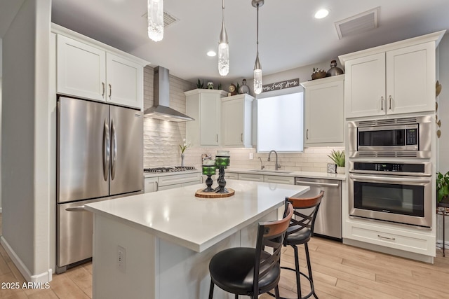 kitchen with a kitchen island, appliances with stainless steel finishes, white cabinetry, sink, and wall chimney range hood