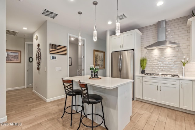 kitchen with white cabinetry, wall chimney range hood, stainless steel appliances, and a kitchen island