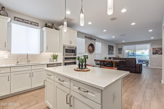 kitchen with sink, appliances with stainless steel finishes, hanging light fixtures, tasteful backsplash, and a kitchen island