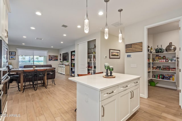 kitchen featuring a center island, light hardwood / wood-style flooring, stainless steel microwave, pendant lighting, and white cabinets