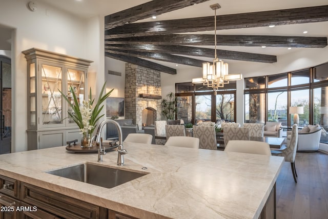 kitchen featuring sink, an inviting chandelier, light stone counters, decorative light fixtures, and beamed ceiling