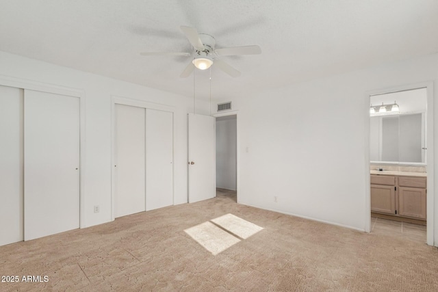 unfurnished bedroom featuring light colored carpet, ensuite bath, visible vents, and multiple closets