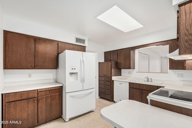 kitchen featuring white appliances, light tile patterned floors, light countertops, dark brown cabinets, and a sink
