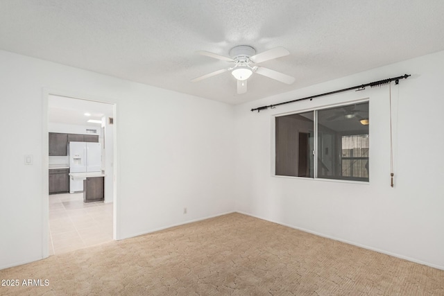 unfurnished room featuring a textured ceiling, light colored carpet, ceiling fan, and baseboards