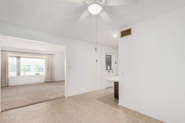 unfurnished room with a textured ceiling, a ceiling fan, visible vents, light carpet, and light tile patterned flooring