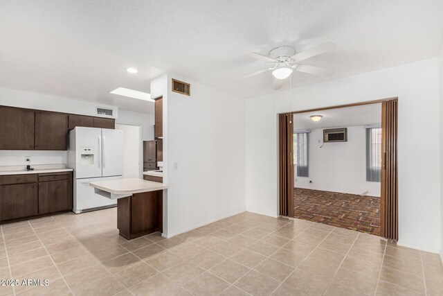 kitchen featuring white refrigerator with ice dispenser, a ceiling fan, light countertops, dark brown cabinets, and visible vents