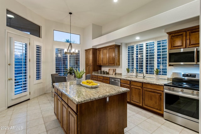 kitchen with a center island, stainless steel appliances, a sink, light stone countertops, and a chandelier