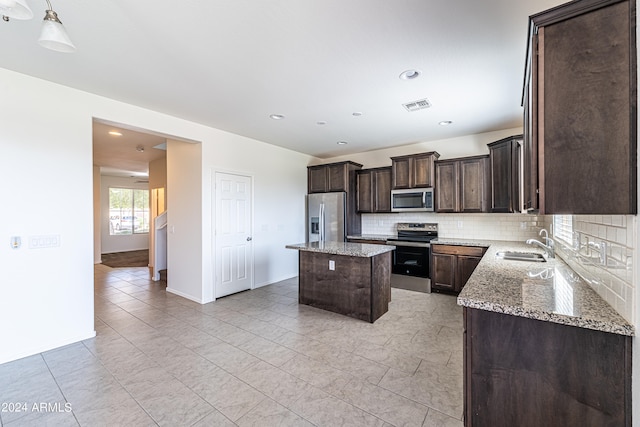 kitchen featuring stainless steel appliances, decorative backsplash, sink, a kitchen island, and light stone countertops