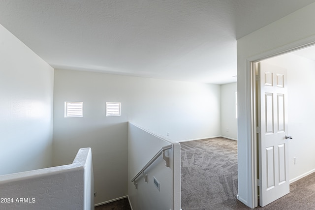 hallway with a textured ceiling and dark carpet