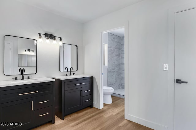 bathroom featuring wood-type flooring, tiled shower, vanity, and toilet