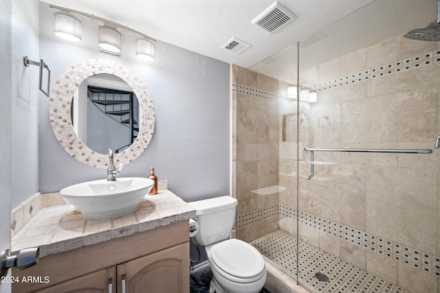 bathroom featuring a textured ceiling, a shower with door, vanity, and toilet