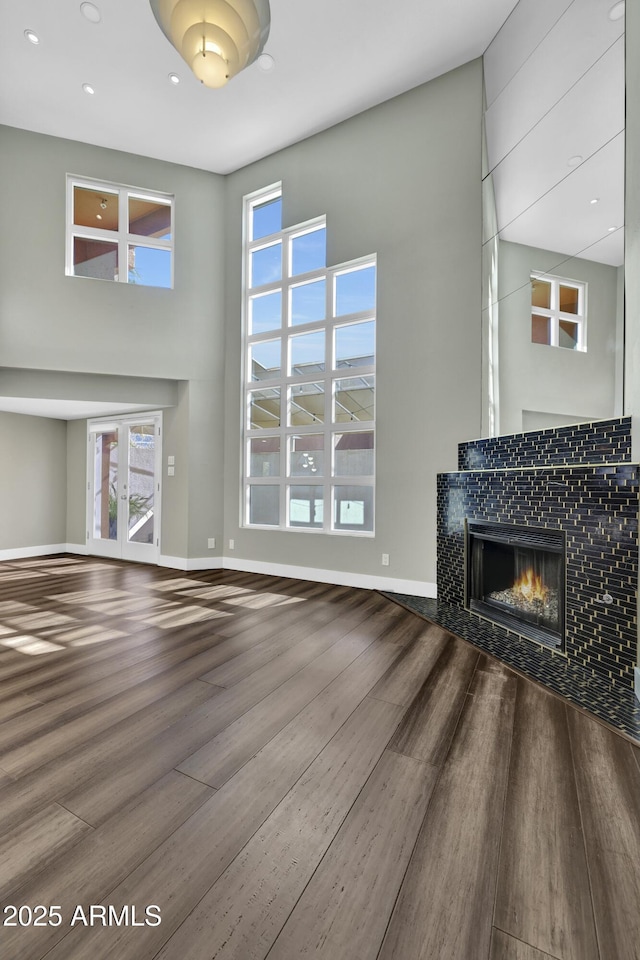 unfurnished living room featuring a high ceiling, hardwood / wood-style floors, and a tiled fireplace