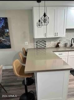 interior space featuring hardwood / wood-style flooring, a breakfast bar area, sink, decorative light fixtures, and white cabinetry