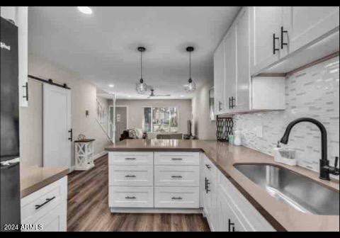 kitchen featuring kitchen peninsula, sink, a barn door, pendant lighting, and white cabinets