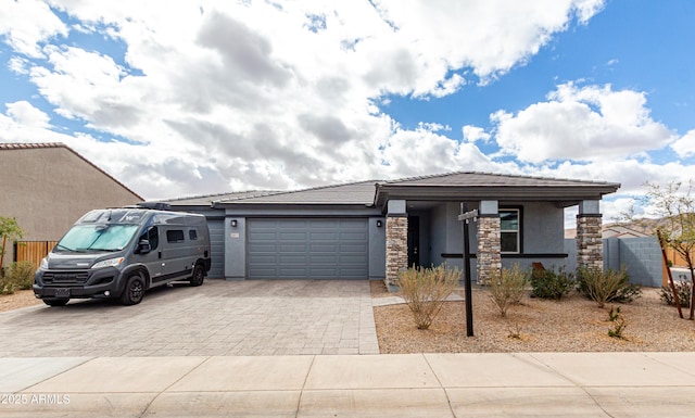 view of front of house featuring decorative driveway, an attached garage, fence, and stucco siding