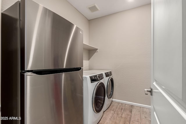 clothes washing area with light wood-style flooring, laundry area, visible vents, baseboards, and washer and clothes dryer