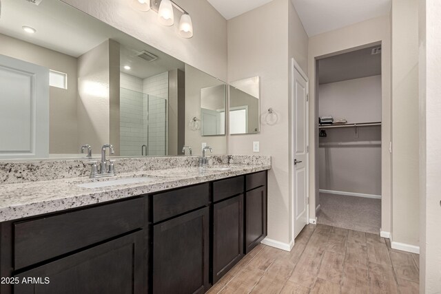 bathroom featuring a shower stall, a walk in closet, a sink, and wood finished floors