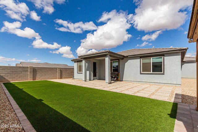 rear view of house with stucco siding, a fenced backyard, a lawn, and a patio