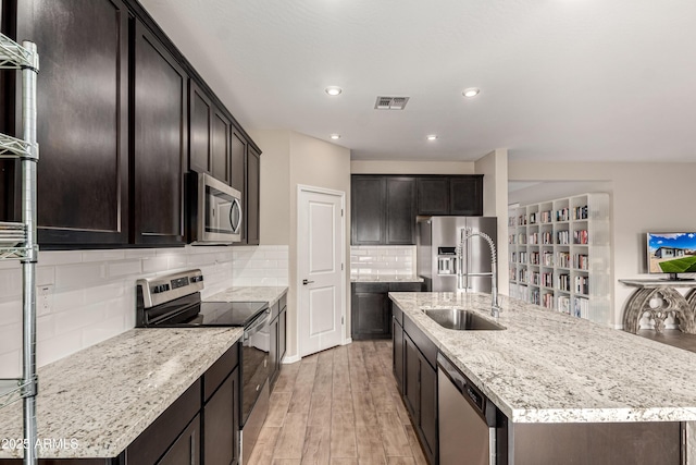 kitchen with light wood finished floors, visible vents, an island with sink, appliances with stainless steel finishes, and a sink