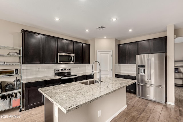 kitchen with stainless steel appliances, visible vents, wood tiled floor, a sink, and light stone countertops