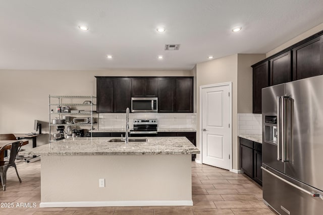 kitchen featuring light stone countertops, visible vents, appliances with stainless steel finishes, and a sink